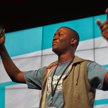 nubi kayode raises his arms as he speaks on stage