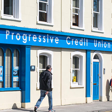 a man walking by a blue credit union sign on his way to open a bank account