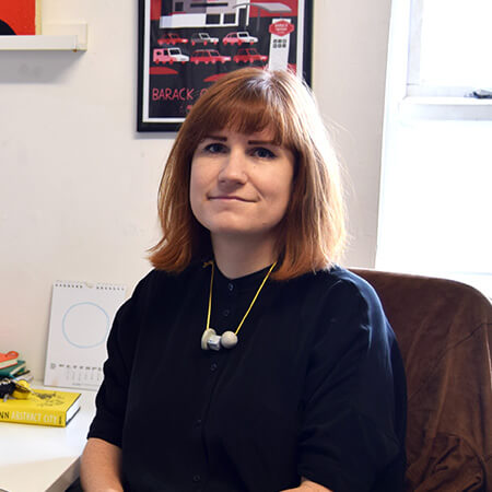 a portrait of fuchsia macaree sitting in her studio wearing a navy jumper