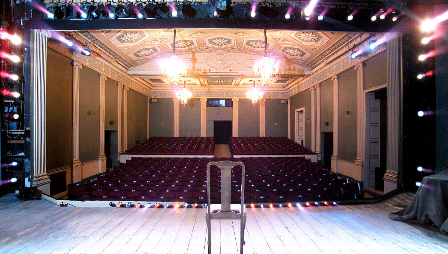 a chair sits in the middle of a brightly lit stage looking out onto hundreds of seats