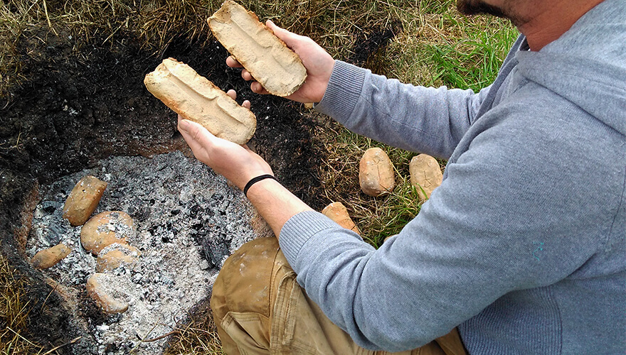 A pit dug into the ground in which coals smoulder. Amongst the ash is some beige-coloured, potato-shaped objects. O'Neill reaches for one and opens it into two halves. It's a mould for a brooch.