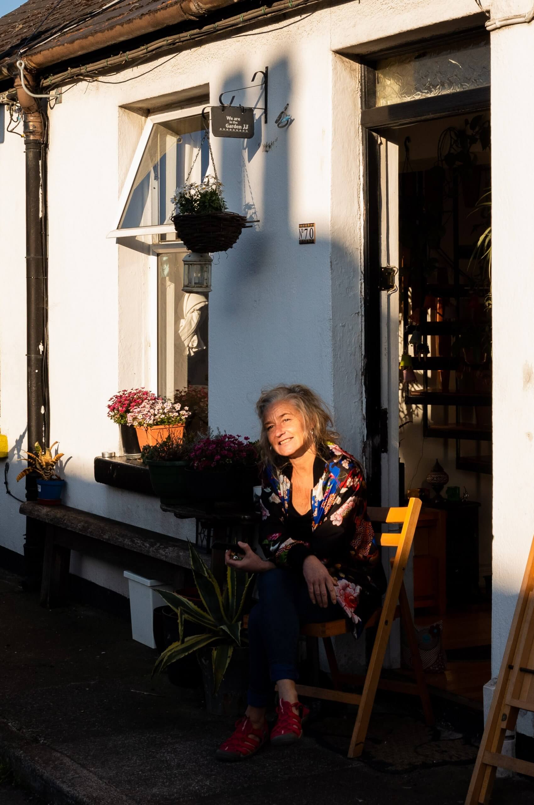 A woman sitting on a chair at her front door. Sunlight crosses her face.