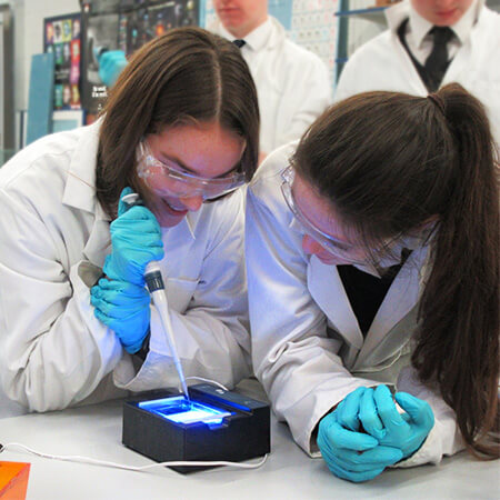 two female pupils from st andrew's private school wear lab coats and goggles