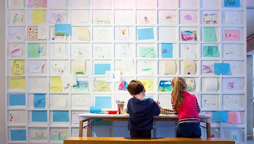 two children stand in front of colourful art and postits that line the walls of the ark