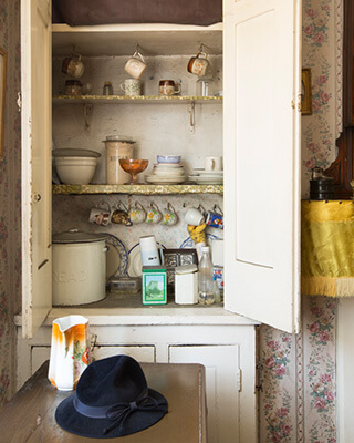 a press at the iveagh trust museum flat filled with hanging cups, a bread bin, a tea box and other tins