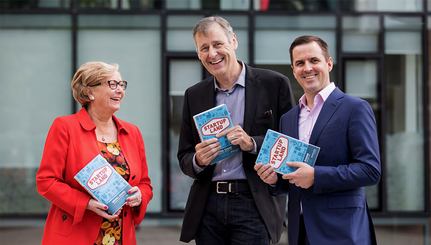 in formal business clothes, three business people smile and pose for the camera